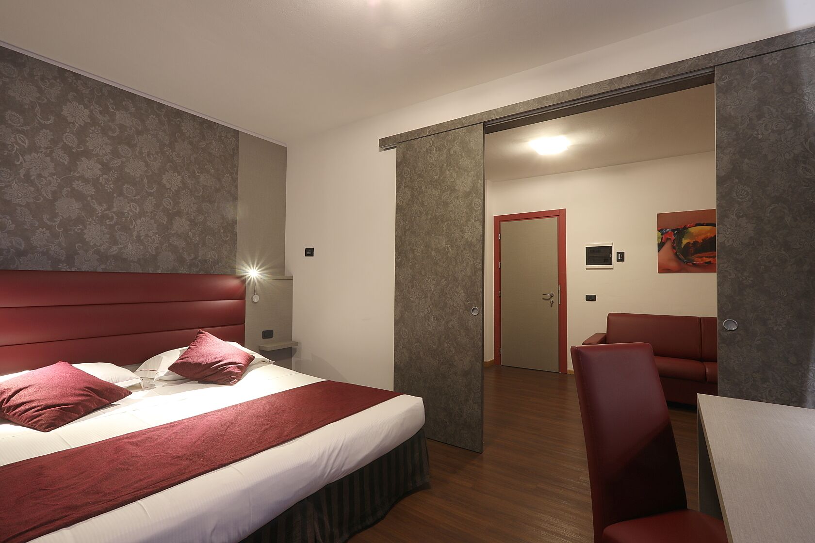 Habitación de hotel con una cama grande, un escritorio y una silla. Se ve una puerta que da a otra habitación.
