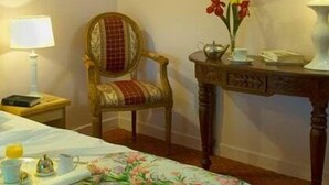 A hotel room with a bed, a chair, a table with a lamp, and a painting on the wall. - LOGIS Chez Bach (Chaussin)
