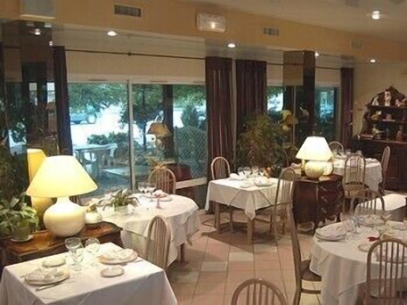 Un restaurant avec des tables rondes dressées pour le repas, chacune étant recouverte d’une nappe blanche et agrémentée d’une lampe.