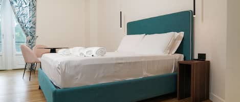 Un dormitorio moderno con una cama color turquesa, ropa de cama blanca, una mesita de noche de madera y una silla.