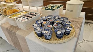 A buffet setup with various food items and containers, including jars of cereal, a basket of biscuits, and a tray of yogurt cups. - Hotel Il Tesoro Pompeiano (Pompei)