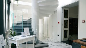 A modern lobby with a marble floor, a white reception desk, and a staircase with glass railings. - Hotel Il Tesoro Pompeiano (Pompei)