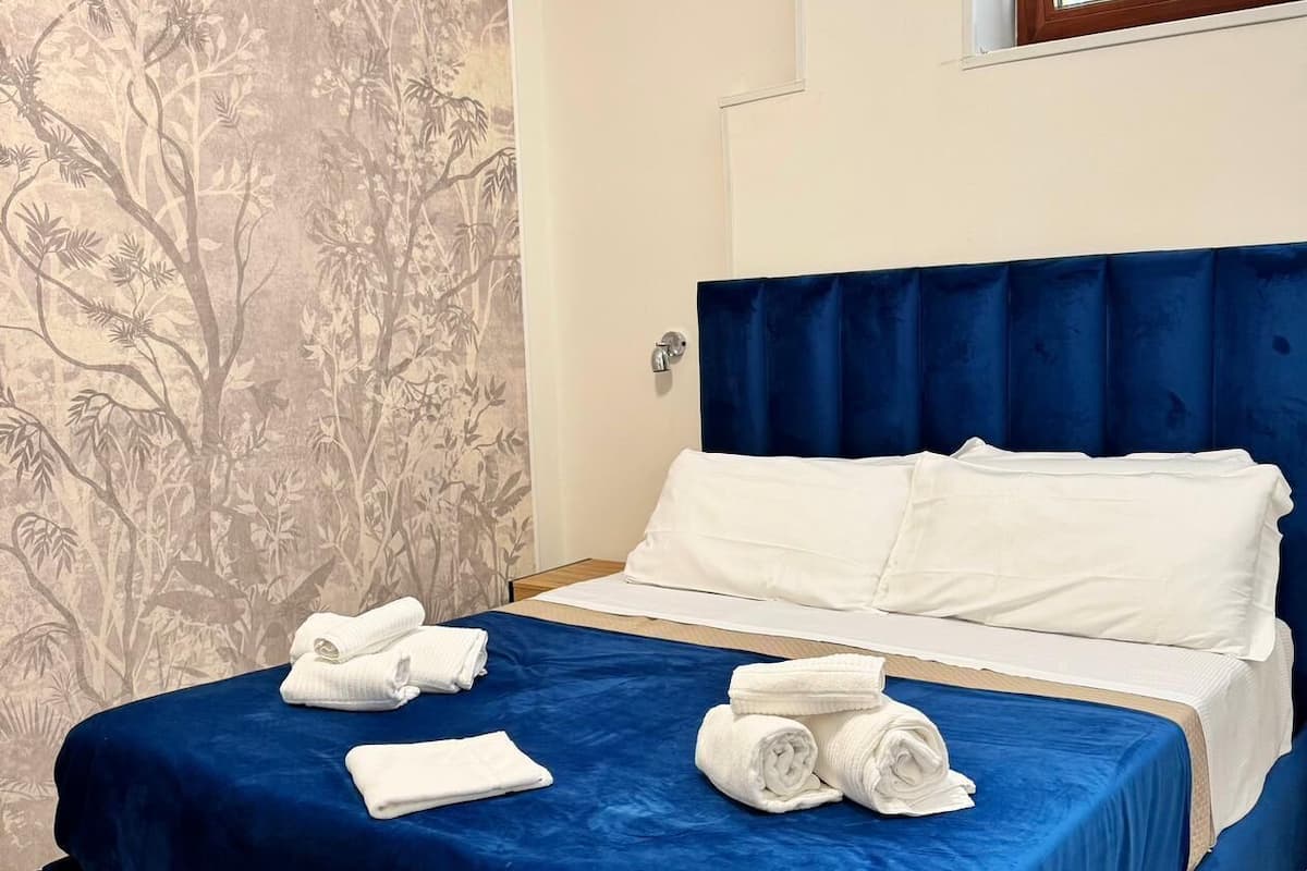 A hotel room with a bed, blue bedspread, white pillows, and towels.