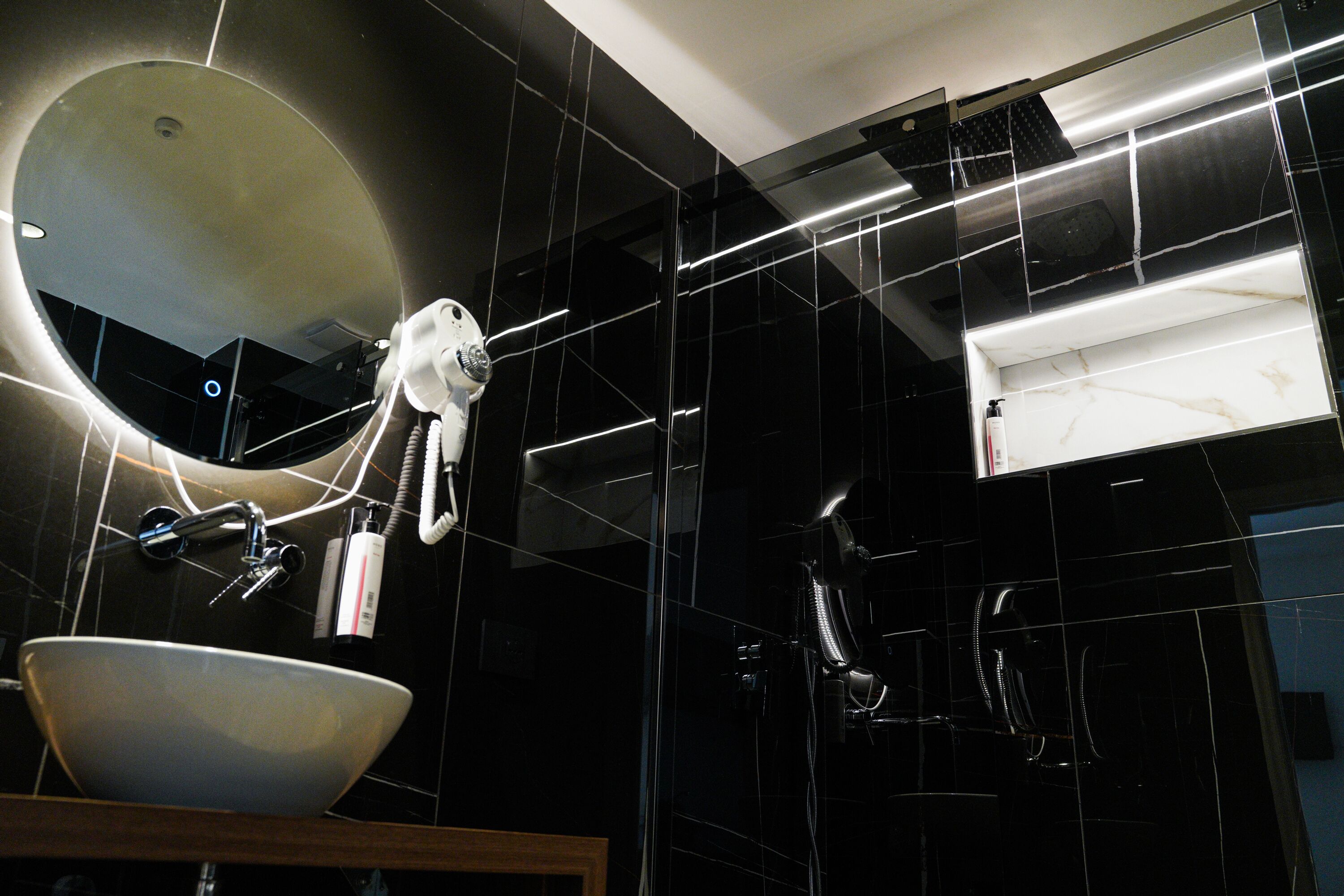 Un baño moderno con un espejo ovalado grande, un lavamanos blanco y un cabezal de ducha de mano.