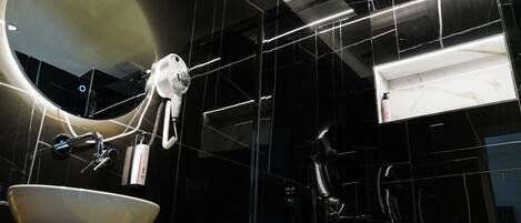 Un baño moderno con un espejo ovalado grande, un lavamanos blanco y un cabezal de ducha de mano.