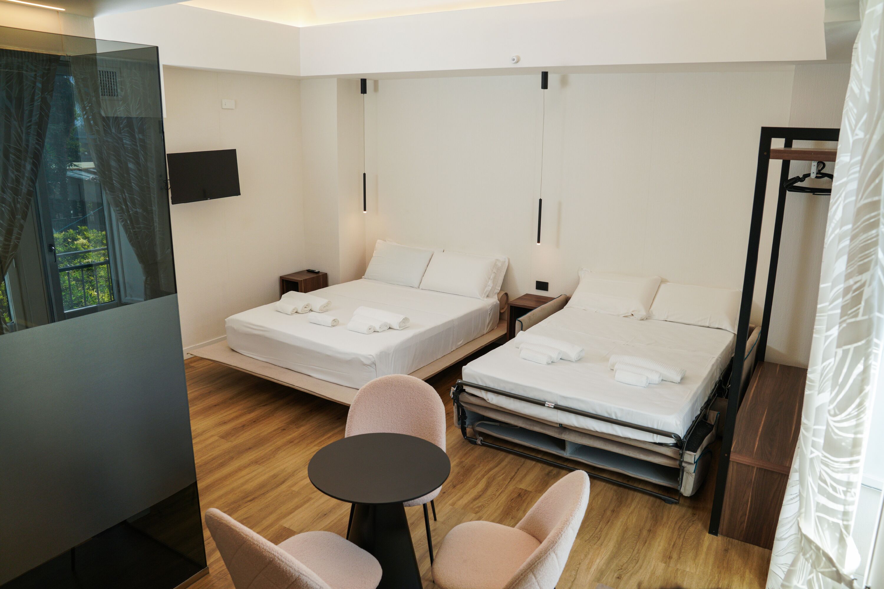 A modern hotel room with two beds, a small table, and a chair.