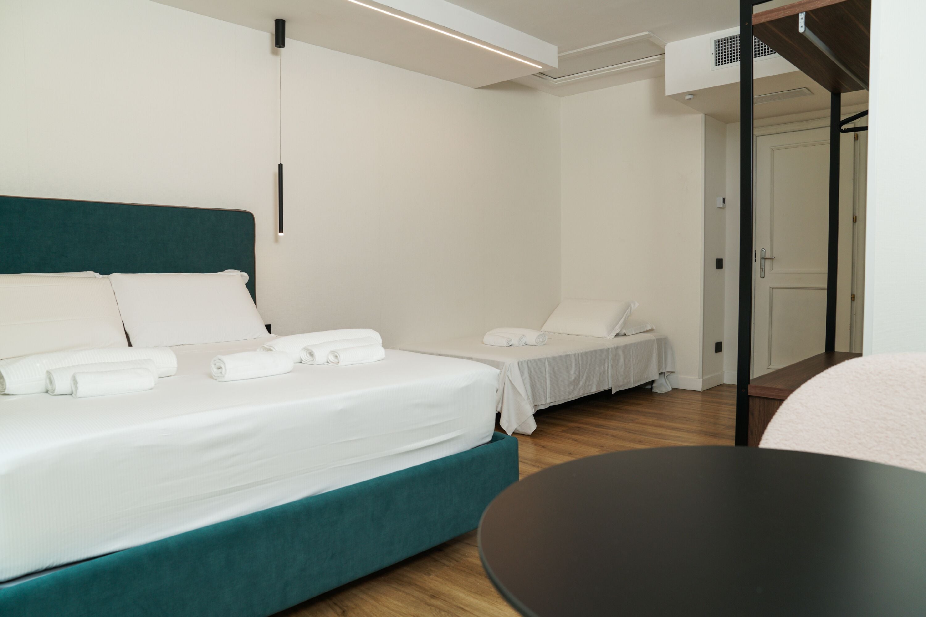 A modern hotel room with a large bed, a smaller bed, a round table, and a door leading to a bathroom.