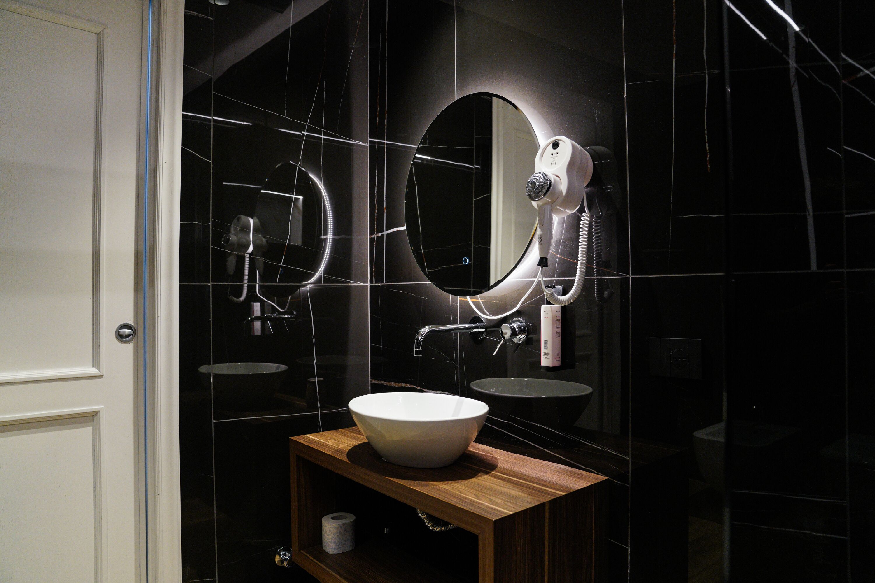 A bathroom with a white sink, a wooden vanity, a large mirror, and a hairdryer.