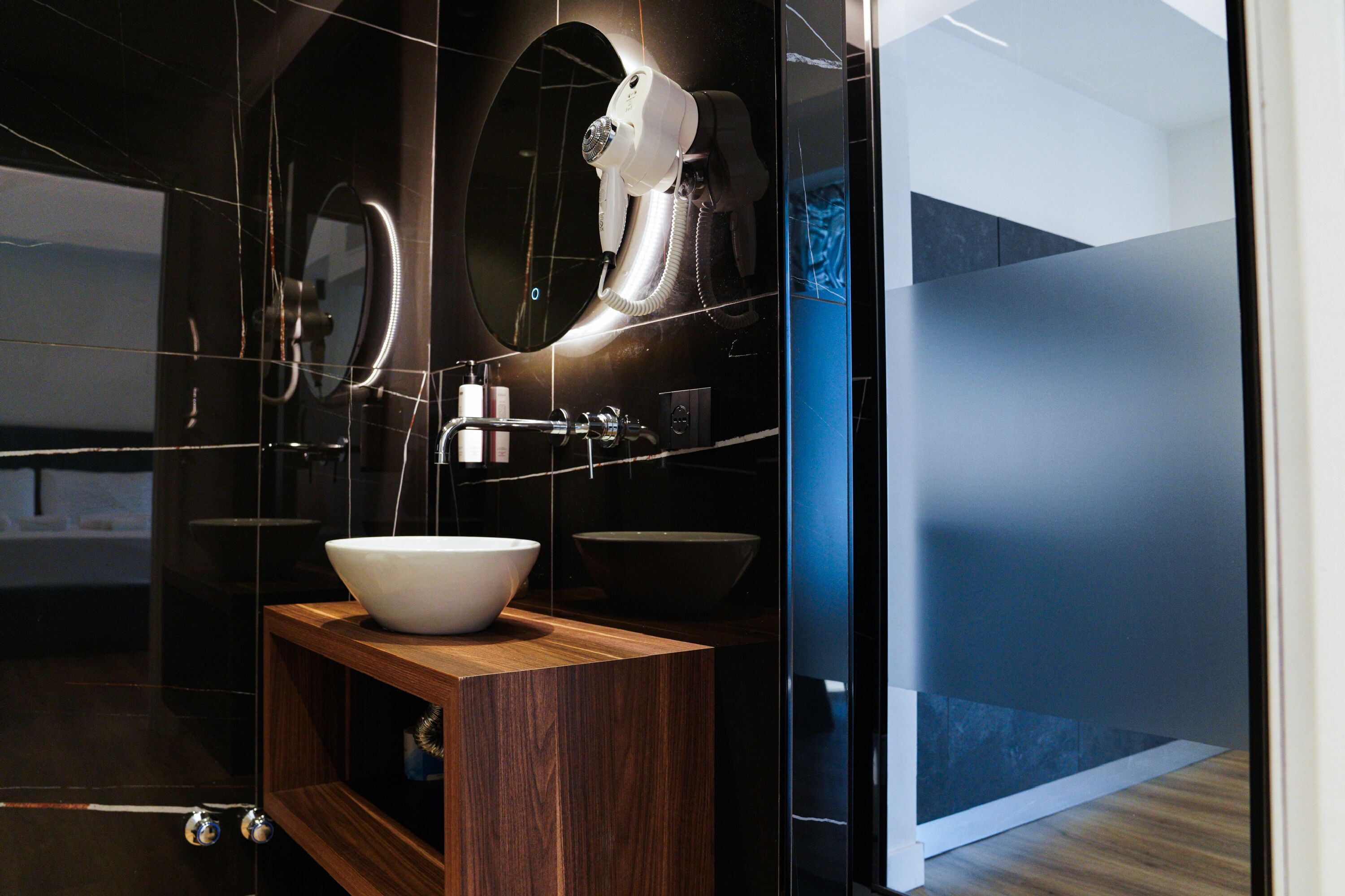 A modern bathroom with a large mirror, a white sink, and a hairdryer mounted on the wall.