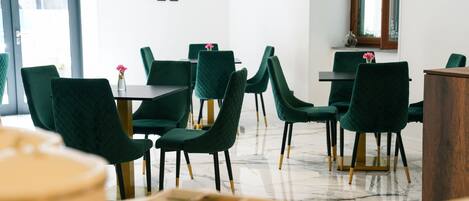 A modern dining area with green upholstered chairs, marble flooring, and a minimalist decor.