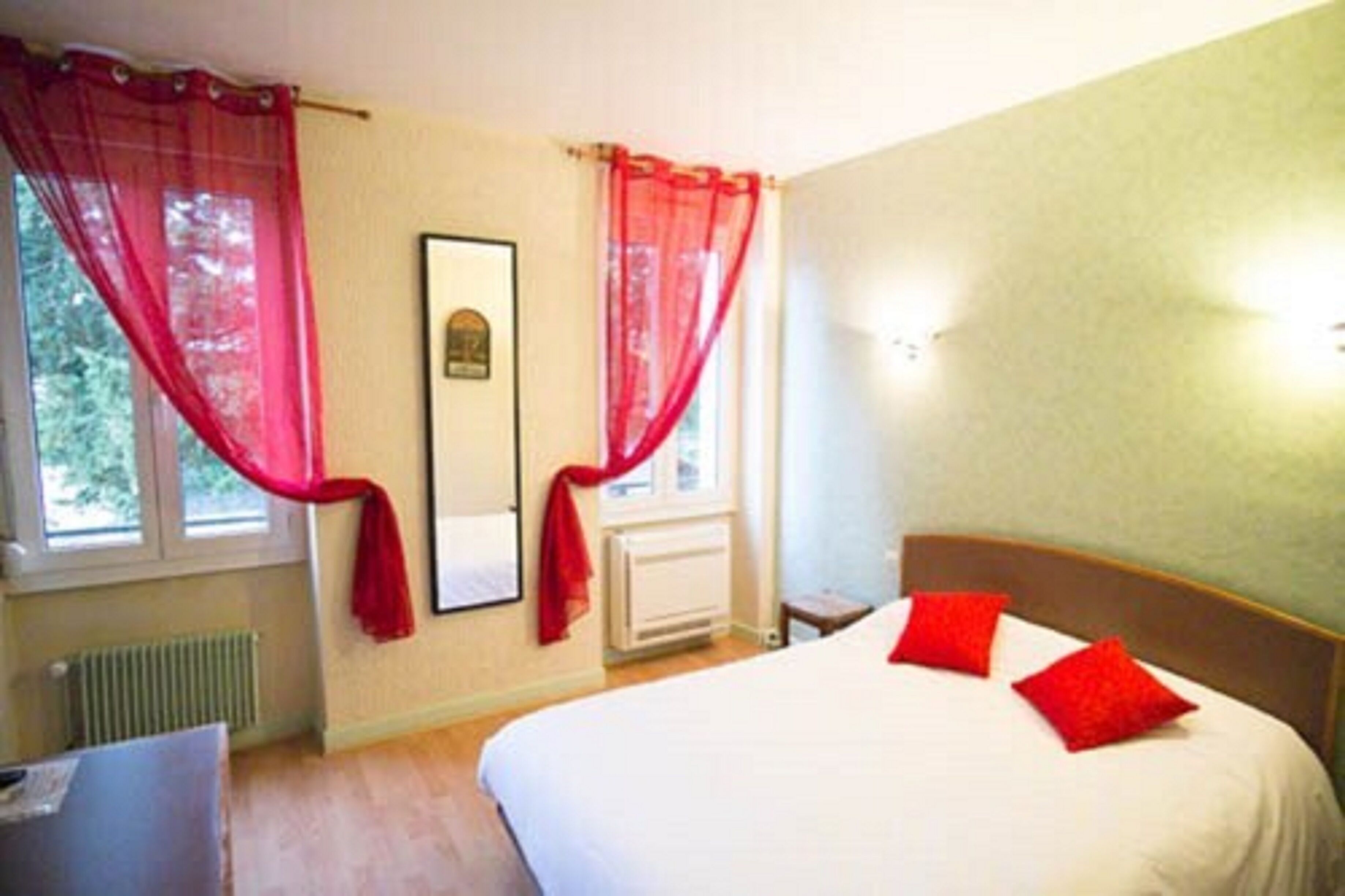 Un dormitorio con cama, cortinas rojas, un cuadro enmarcado y un radiador.