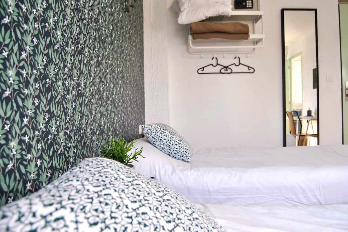 A bedroom with two beds, a hanging towel rack, and a mirror.