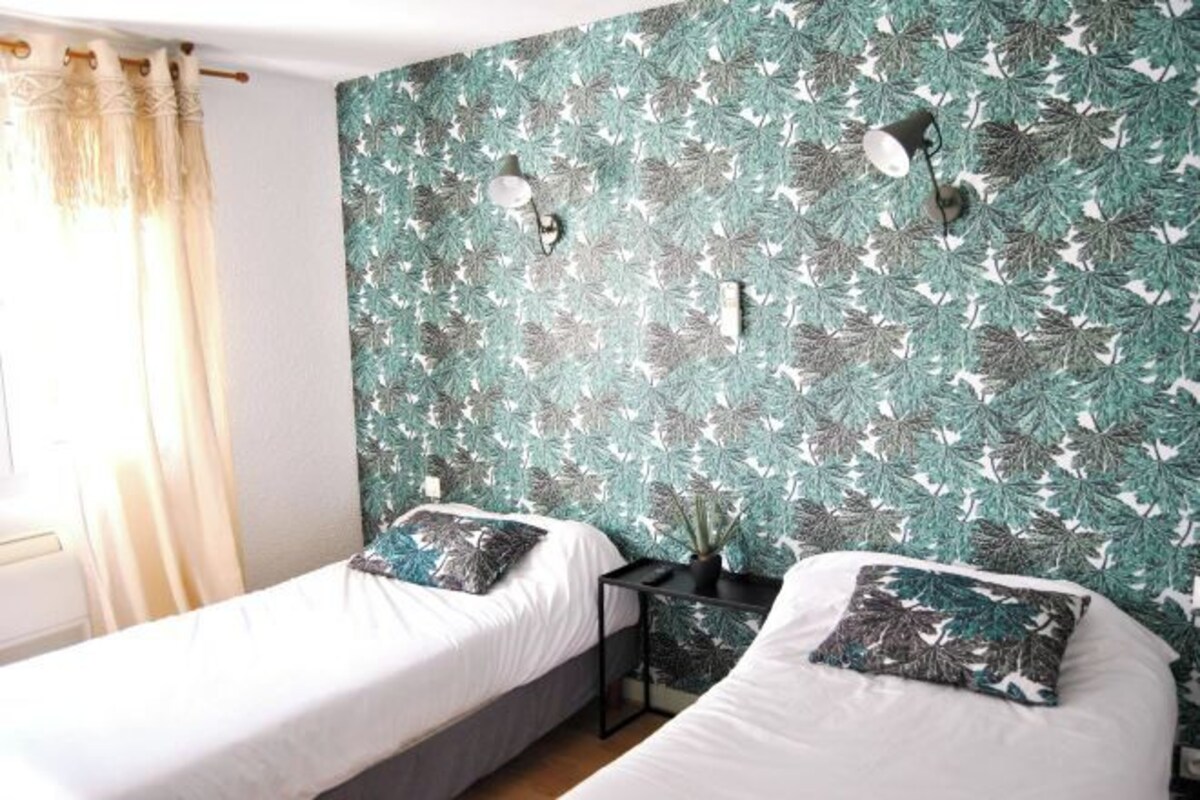 A room with two beds, a nightstand, and a wall with a leafy pattern.