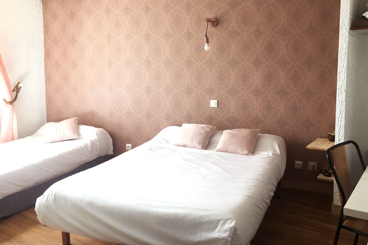 A bedroom with two beds, a nightstand, a chair, and a wall-mounted light fixture.