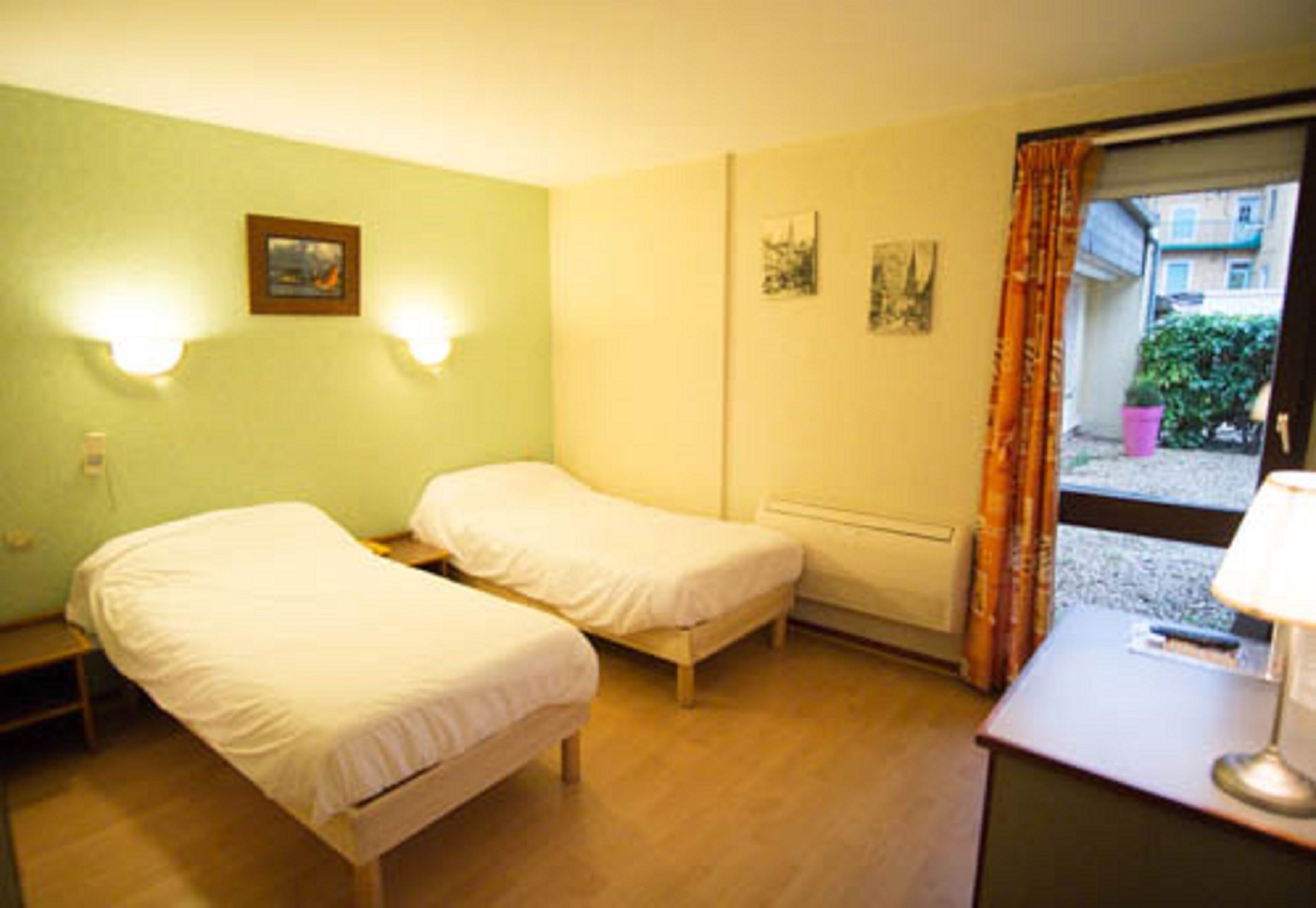 A room with two single beds, a desk with a lamp, and a window with curtains.