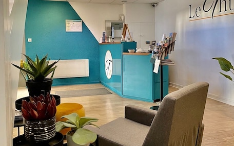 A lobby with a teal wall, a reception desk, a seating area with a chair, and a potted plant.
