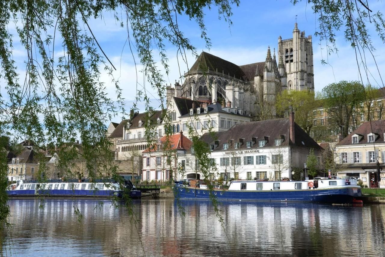 Un edificio histórico con una torre destacada, un río con barcos y edificios residenciales circundantes.