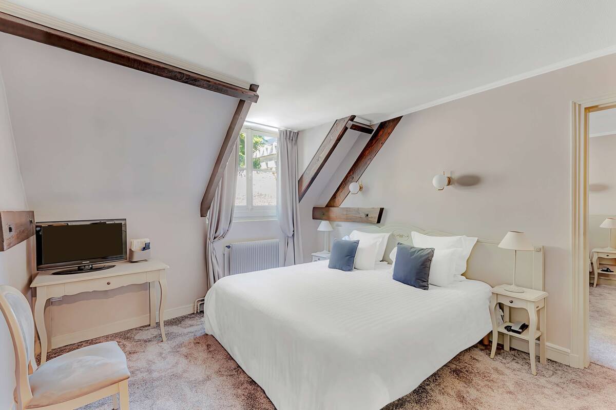 Un dormitorio con una cama grande, un escritorio con computadora, una silla, una lámpara y una ventana con cortinas.