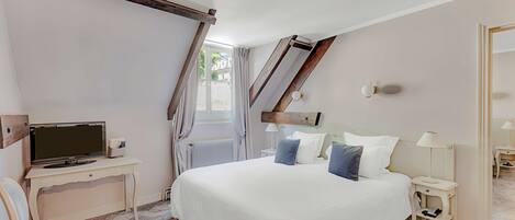 Une chambre à coucher avec un grand lit, un bureau avec un ordinateur, une chaise, une lampe et une fenêtre avec des rideaux.