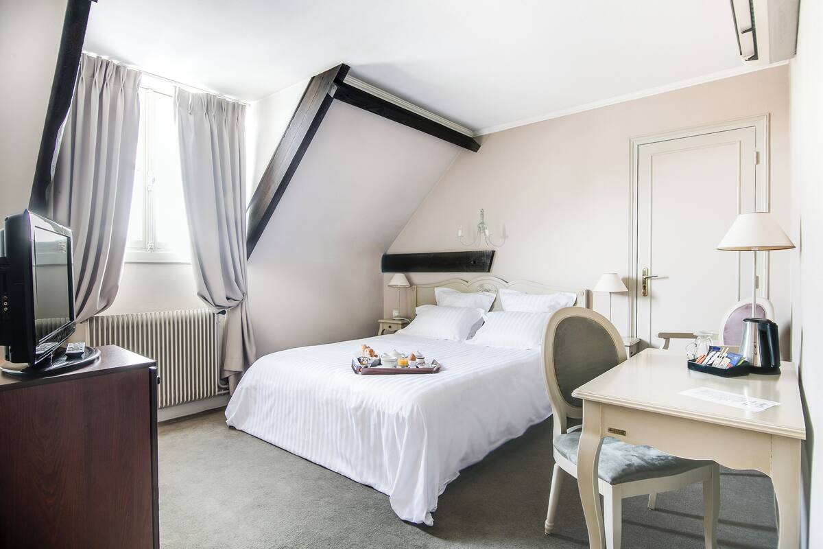 Habitación de hotel con cama, escritorio, silla, televisor, radiador y cortinas.