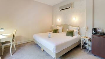 A neatly arranged hotel room with a bed, bedside table, lamp, and a small desk with a chair.