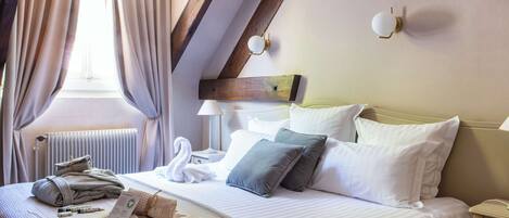 Habitación de hotel con cama, toallas, una decoración con forma de cisne, lámpara y ventana con cortinas.