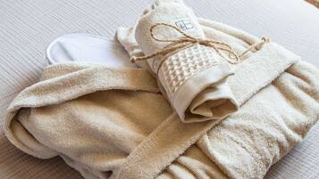 A neatly folded towel and a bottle on a bed with a textured white cover.