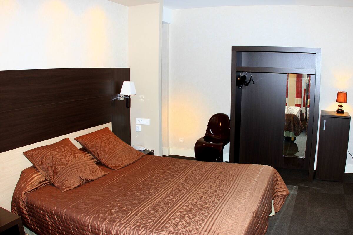 Une chambre d’hôtel avec un grand lit, une tête de lit en bois, une lampe de chevet et une armoire.
