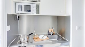 Een kleine keuken met een magnetron, spoelbak en basis keukengerei.