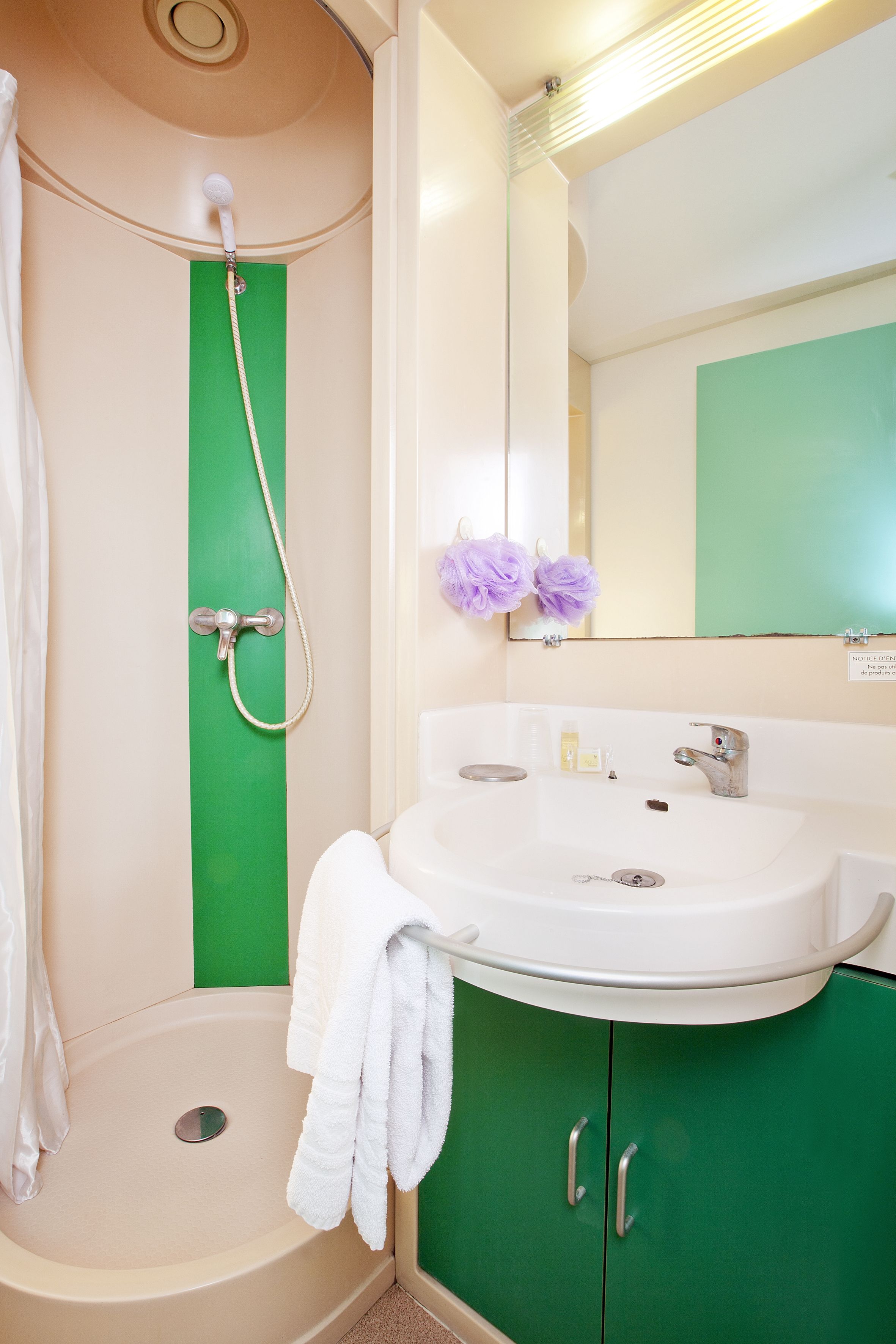 Un baño con cabina de ducha verde, un lavabo blanco y un espejo encima.