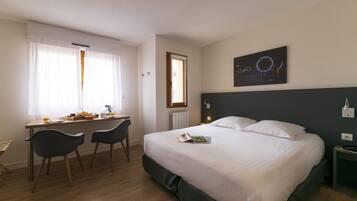 Habitación de hotel con cama, escritorio con sillas, ventana con cortinas y una obra de arte en la pared.