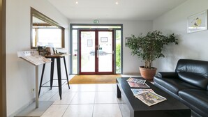 Een receptiegedeelte met een balie, een zwarte leren bank, een plant in pot en een groot raam.