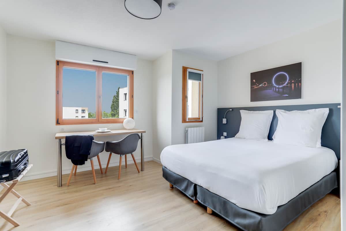 Una habitación de hotel con cama, escritorio, sillas y ventana con vistas.