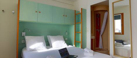 A hotel room with a bed, a laptop, towels, a bathroom with a shower, and a mirror.