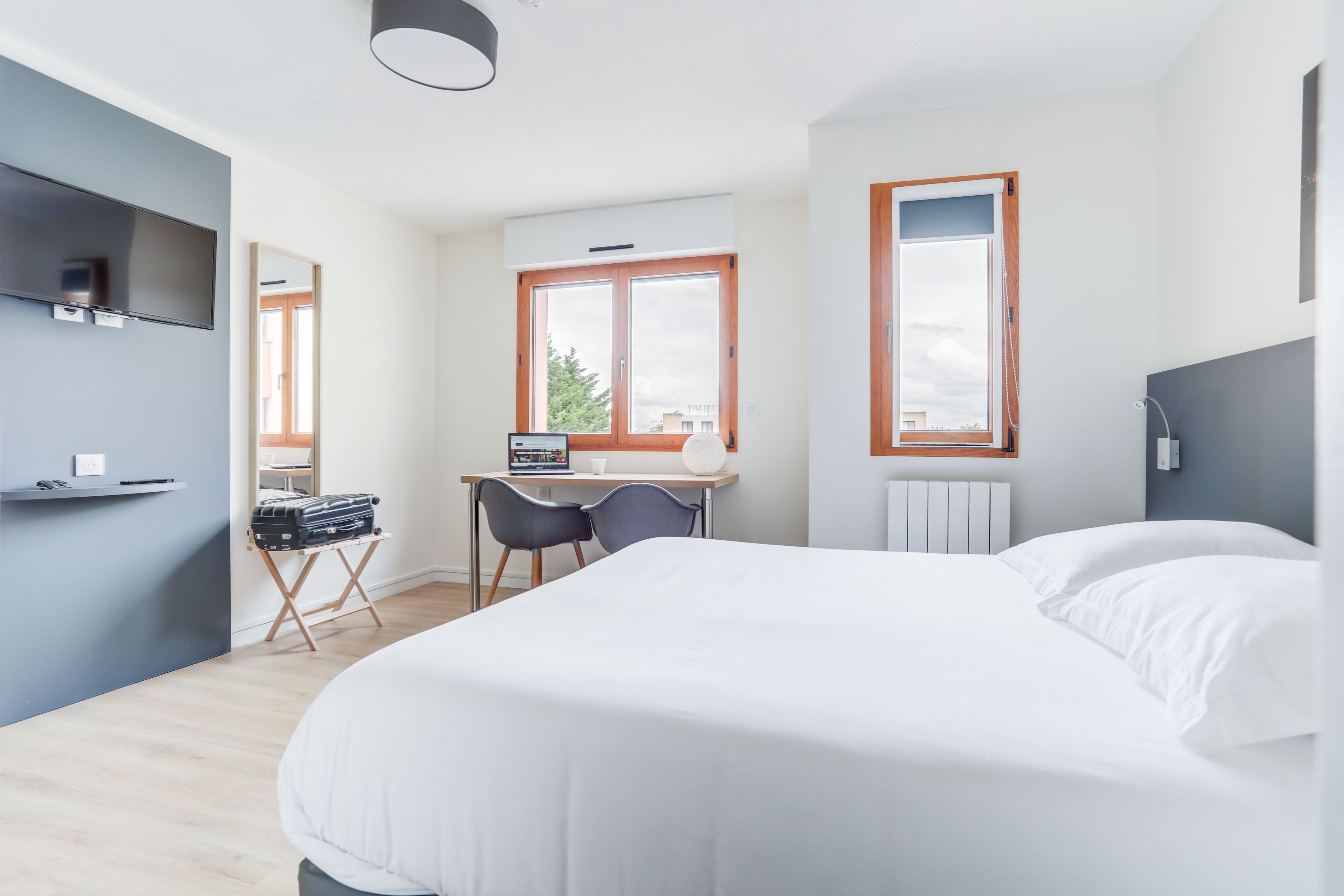 Ein modernes Hotelzimmer mit einem großen Bett, einem Schreibtisch mit Stuhl, einem Fernseher und einem Fenster mit Blick ins Freie.