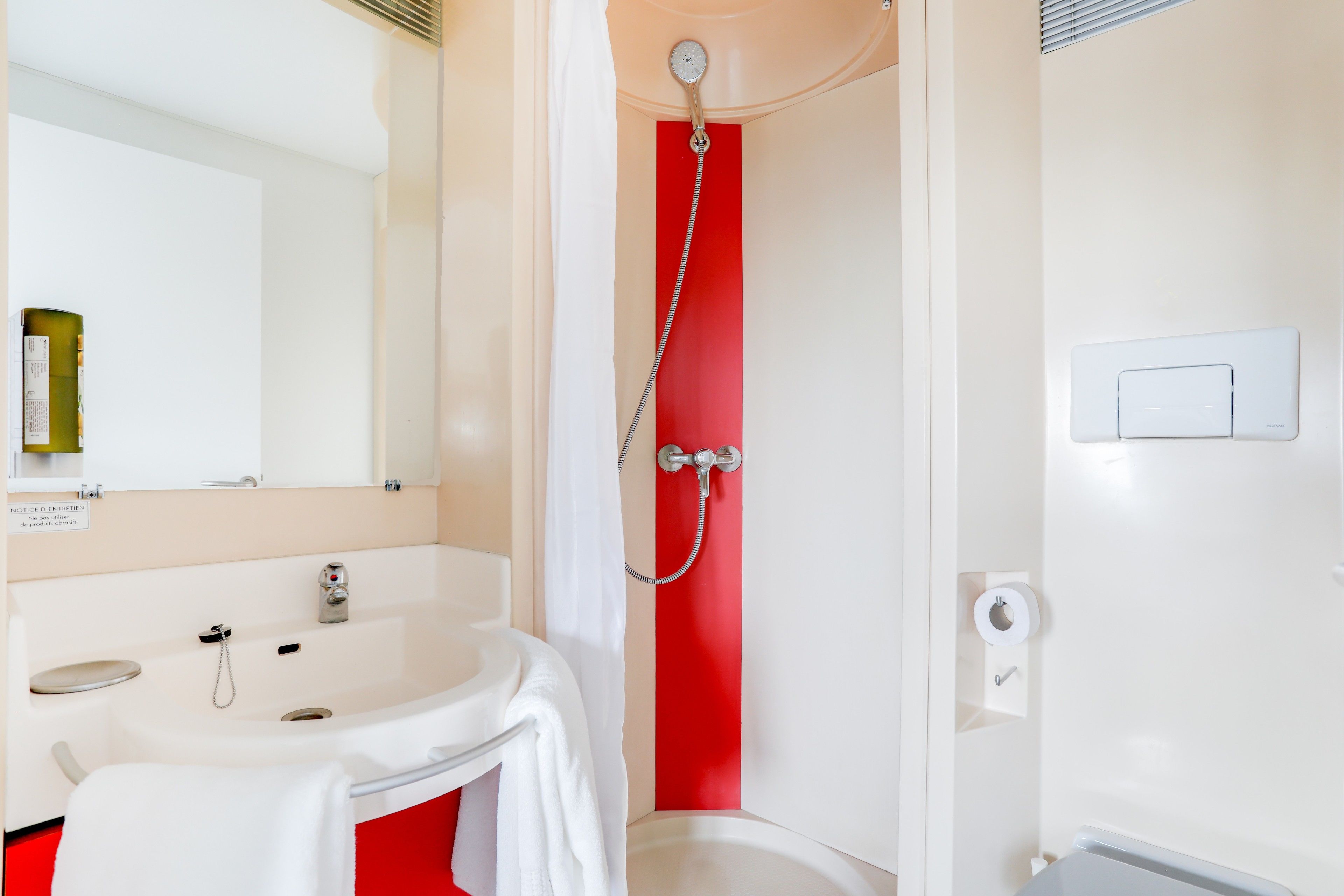 A bathroom with a white sink, a mirror, a red shower wall, and a white toilet.