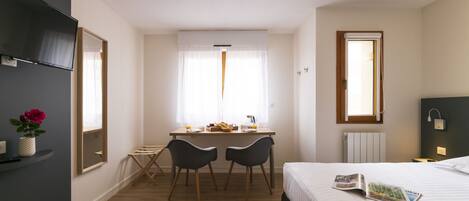 A hotel room with a bed, a desk with two chairs, a television, and a window with curtains.