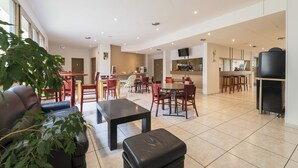 Een ruime woonkamer met een bank, een salontafel en een eettafel met stoelen. Achtergrond toont een keuken met een televisie en een koelkast.