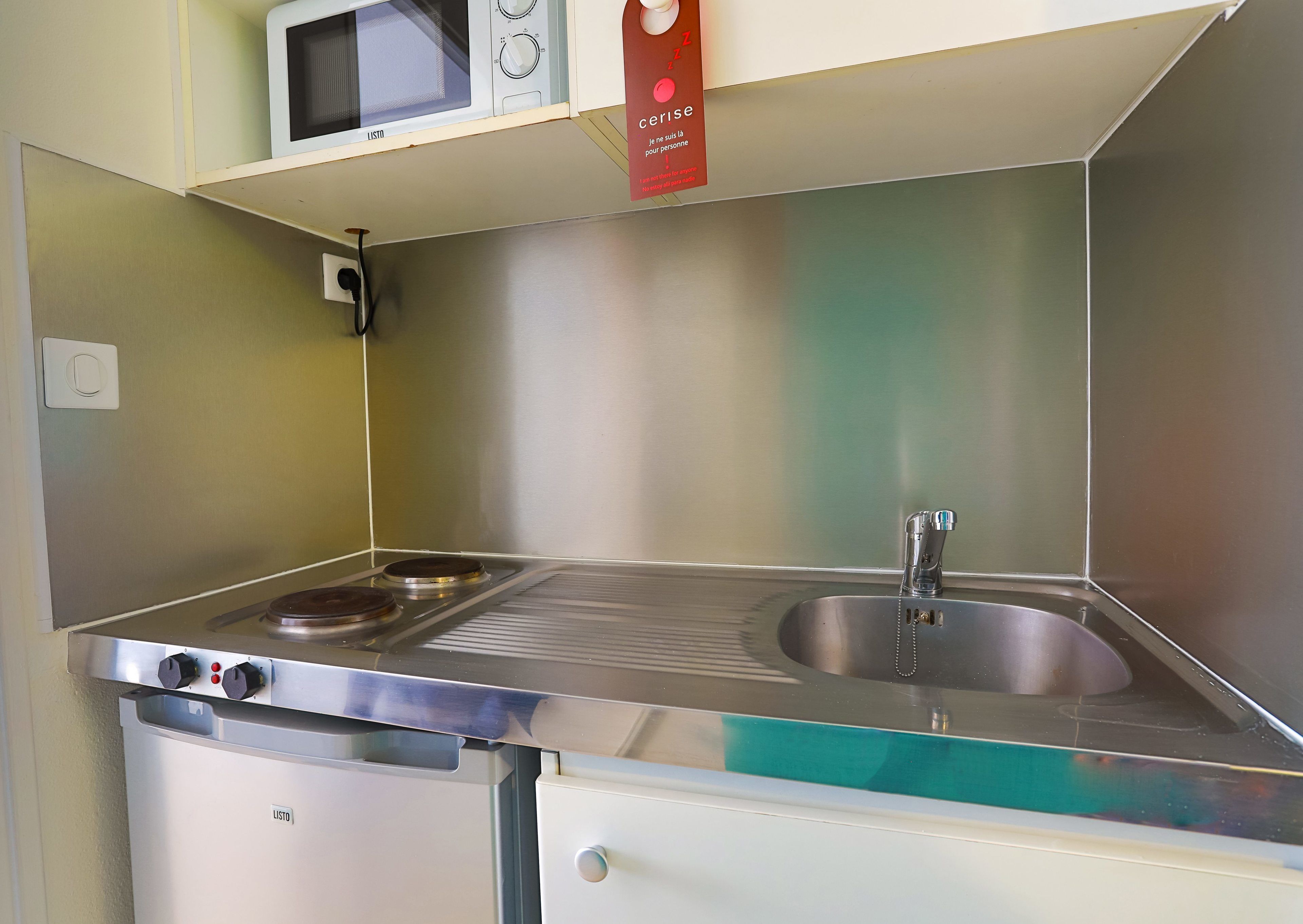 A compact kitchenette with a microwave, stove, sink, and a small cabinet.