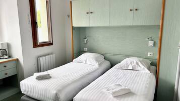 A room with two single beds, a small table with a coffee maker, and a window with blinds.