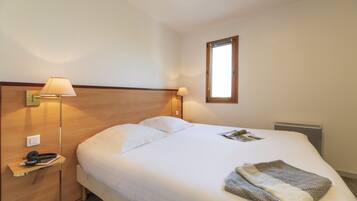A neatly made bed with white linens, a bedside lamp, and a magazine on the bed.