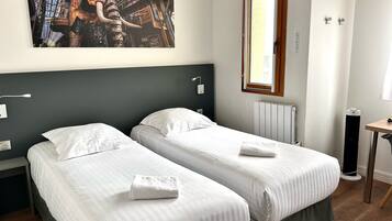 A hotel room with two beds, a large window, a radiator, and a painting on the wall.
