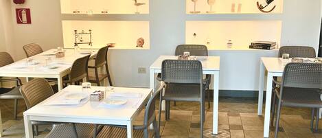 A hotel dining area with tables and chairs, a fire extinguisher, and decorative items on shelves.