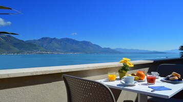 Una tavola imbandita con cibi per la colazione, un vaso di fiori e vista su un paesaggio costiero con montagne.