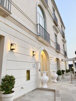 Esterno di un hotel con facciata classica, portici ad arco e area salotto all'aperto con piante in vaso.