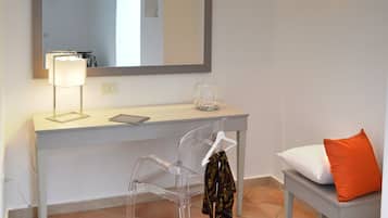 A bathroom with a white vanity, a mirror, a wall-mounted light, a chair, and a bench with an orange pillow.