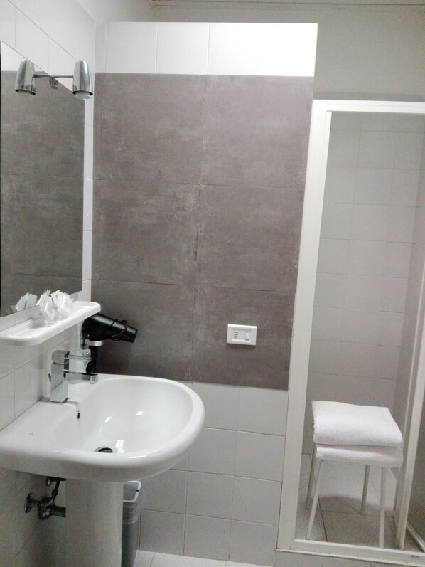 Un baño con un lavabo blanco, un espejo, toallero y zona de ducha.
