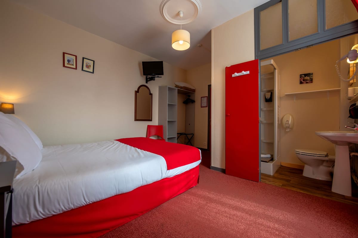 A hotel room with a bed, a television, a red door, a bathroom, and a sink.