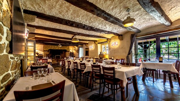 A restaurant with stone walls, wooden beams, and tables set for dining. - Logis Auberge de Kerveoc'h (Douarnenez)