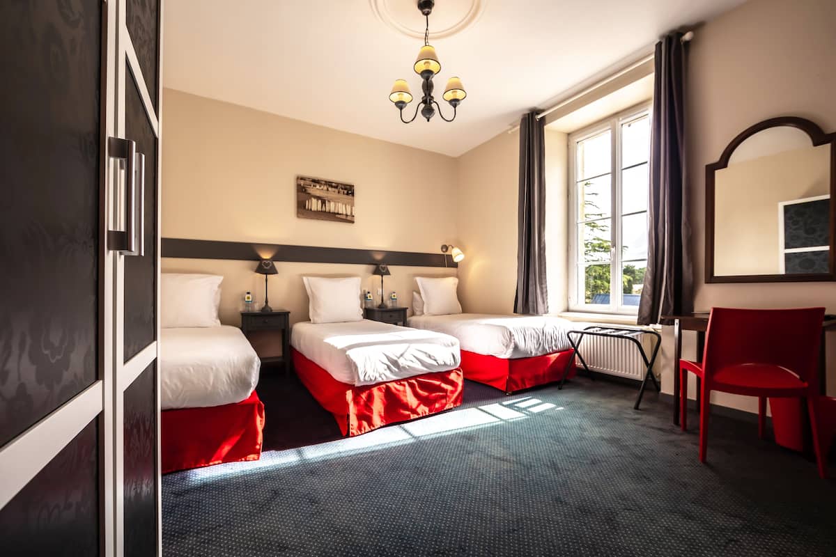 A hotel room with two beds, a red chair, a desk, a mirror, and a window with curtains.